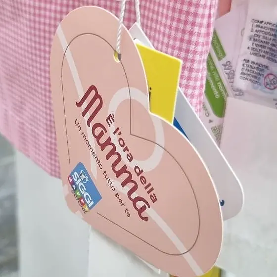 Cartellino a forma di cuore con la scritta È l'ora della mamma appeso a un grembiule a quadretti rosa