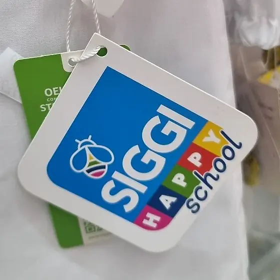 Cartellino del marchio SIGGI Happy School applicato su un grembiule bianco