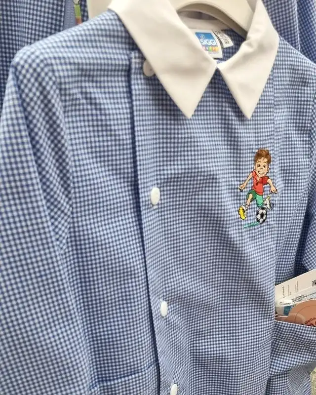Grembiule a quadretti azzurri e bianchi con colletto a punta bianco e ricamo di un bambino che gioca a calcio