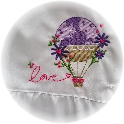 Ricamo di una mongolfiera lilla con fiori e la scritta love, su grembiule bianco